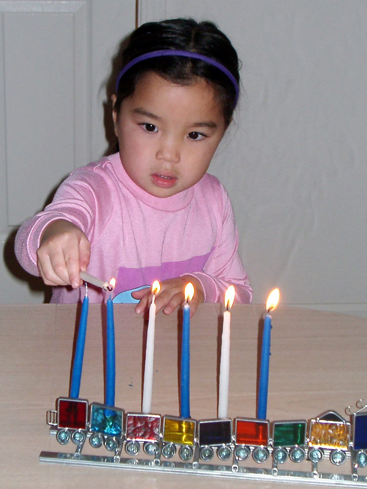 Young girl lighting hannukah candles on a train-motif hanukkiah.