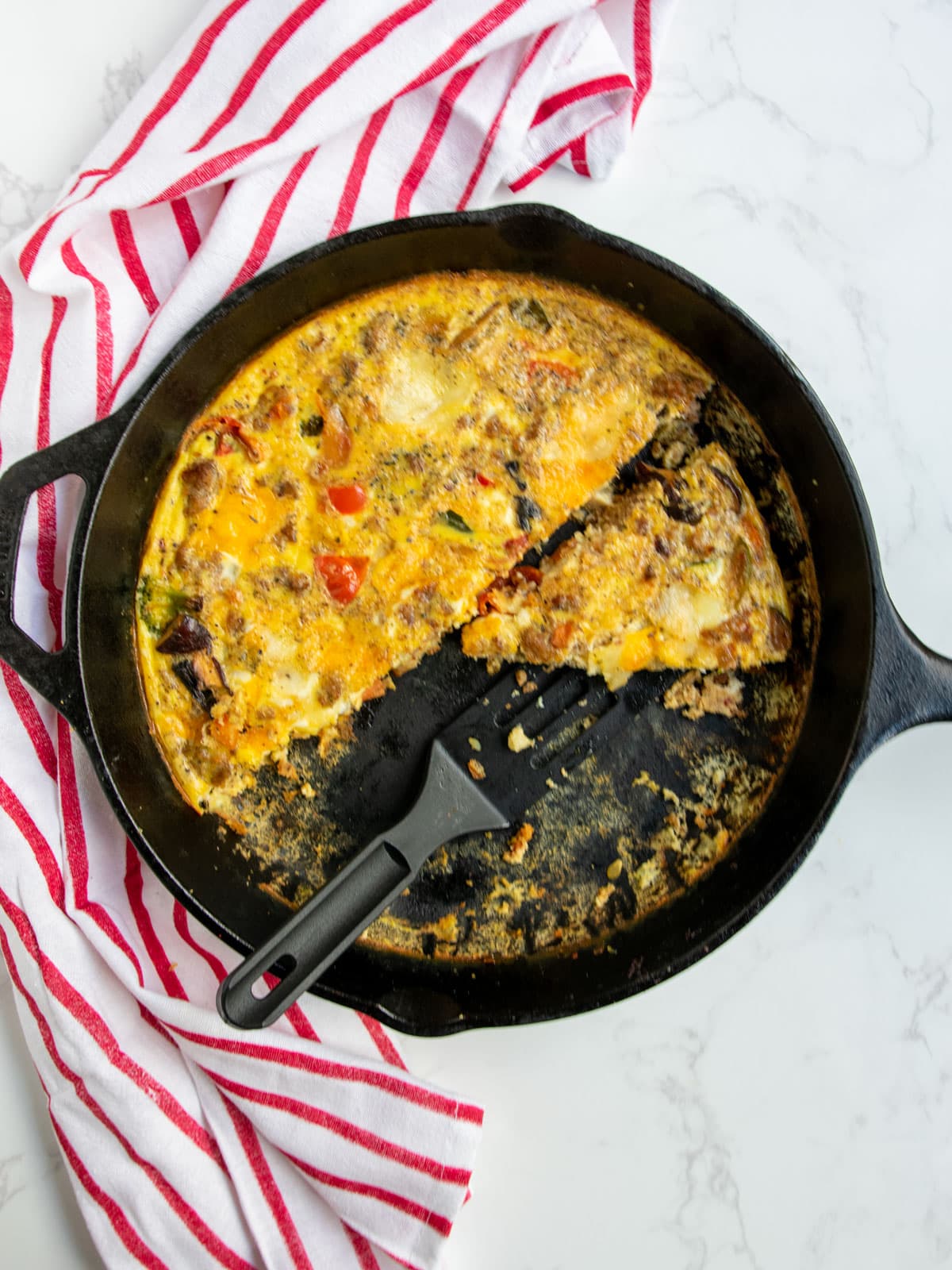 Frittata in a cast iron pan with a black spatula partially cut with a red striped napkin in the background.