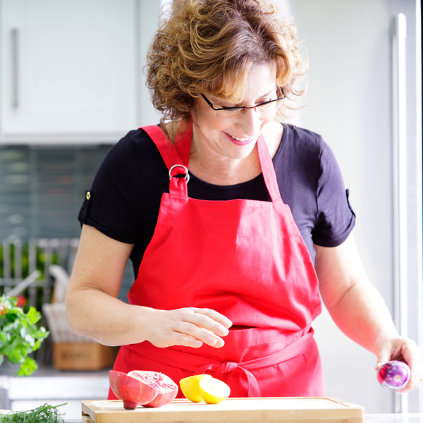 Beth Lee in red apron looking at vegetables on cutting board