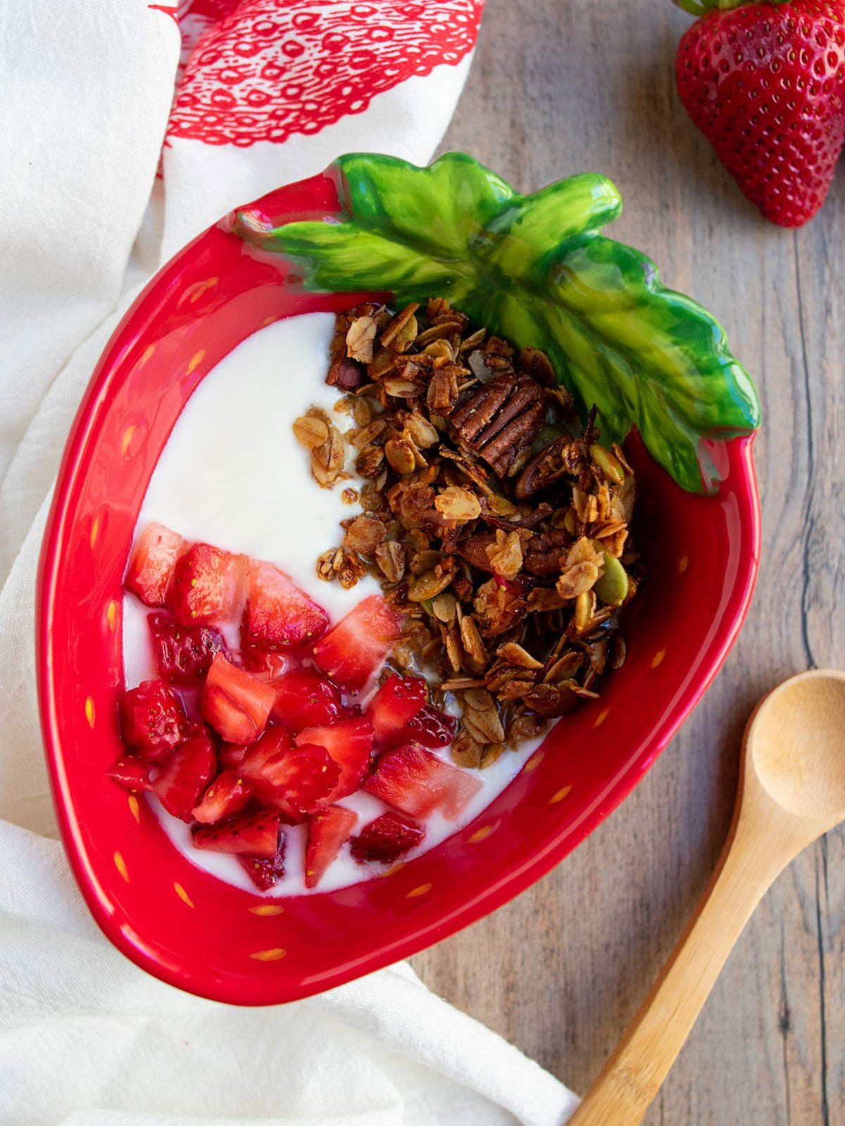 Olive oil granola in a strawberry shaped bowl with yogurt and fresh strawberries.