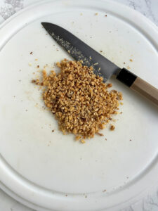 White cutting board with a Japanese knife next to a pile of chopped nuts.