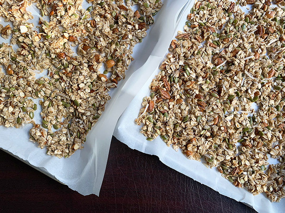 Uncooked granola spread on two sheet pans side by side.