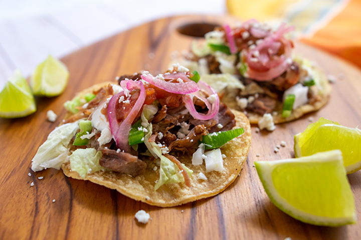 2 carnitas tacos on wooden cutting board with limes.
