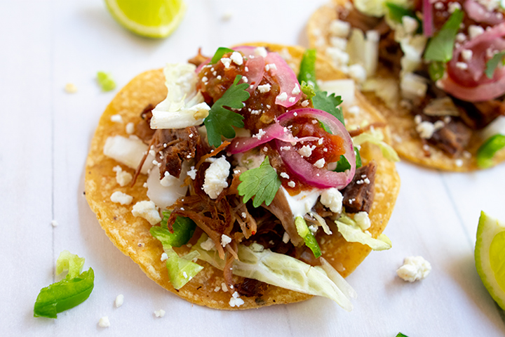 Close up of carnitas tacos on white background with limes.