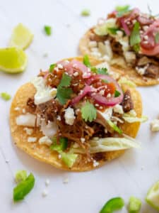 Instant pot carnitas tacos on a white background with limes on the side.