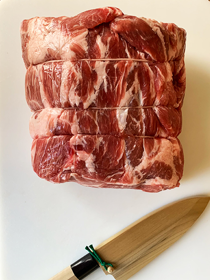 A whole pork butt on cutting board with knife.