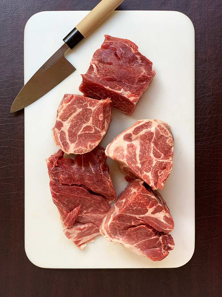Chunks of pork roast on white cutting board with knife.