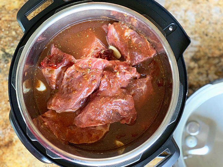 Pork butt in instant pot with sauce poured over it.