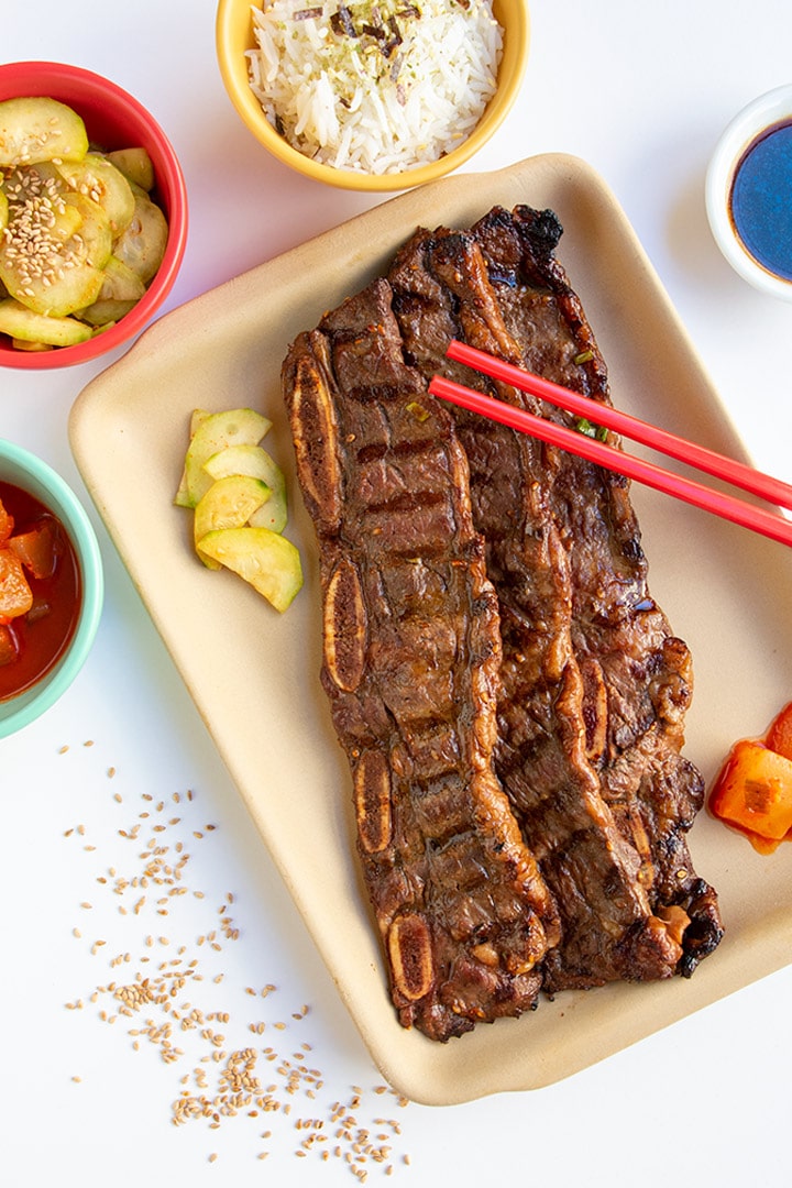 Plate of korean short rib with red chopsticks and cucumber salad, kimchi and rice.