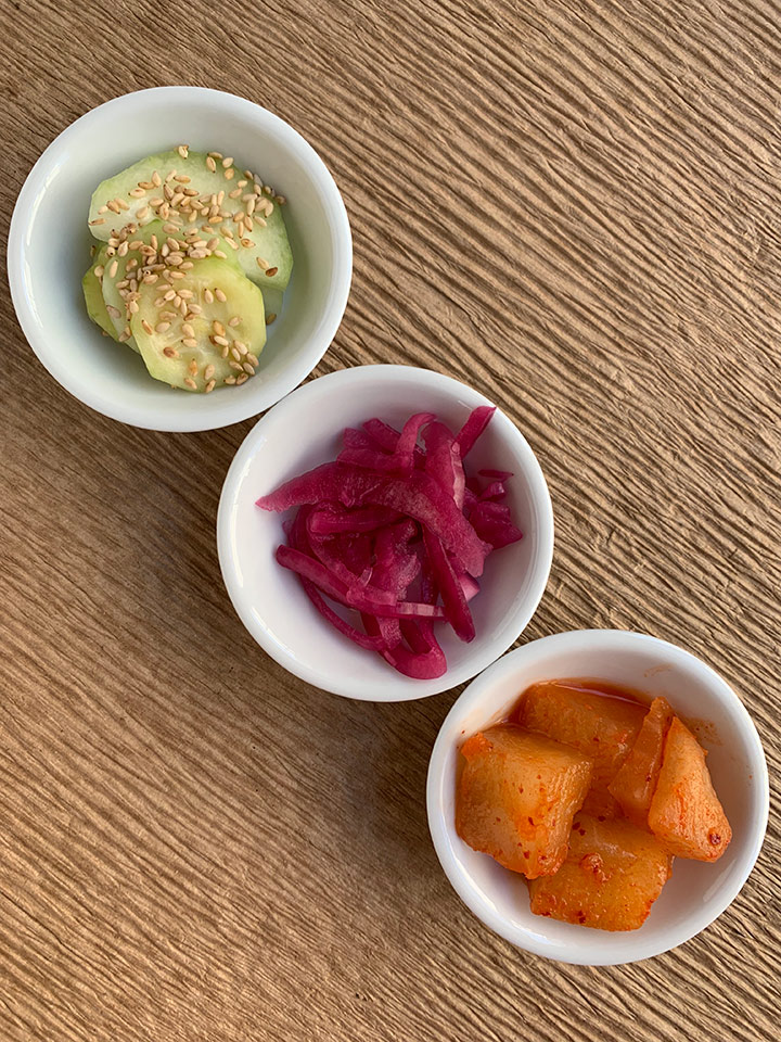 3 types of Korean banchan (side dishes) in small white bowls on corrogated cardboard.