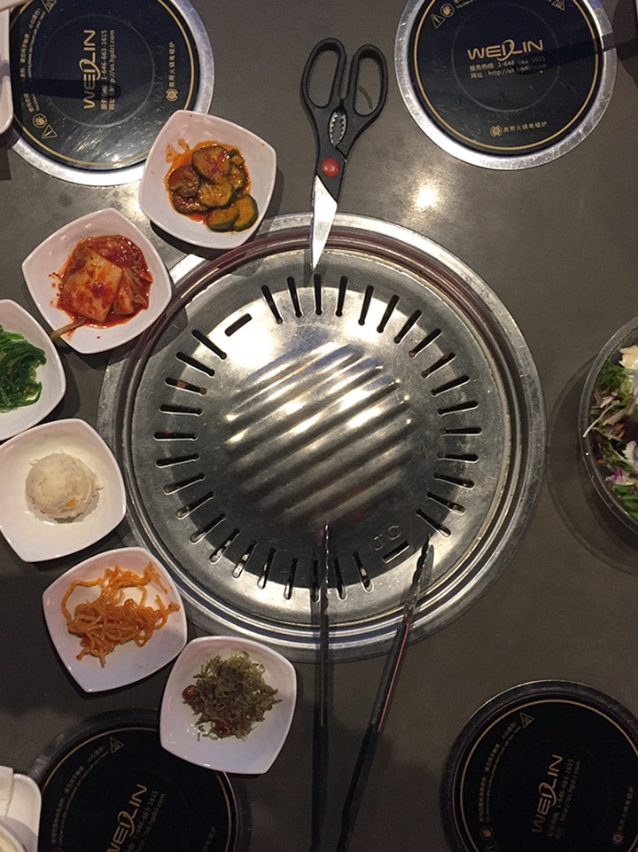 A table top shot of a restaurant bbq in a Korean restaurant with side dishes.