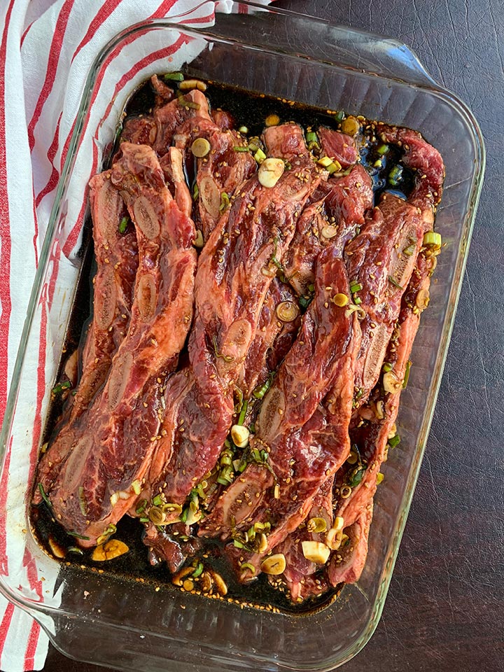 Kalbi style ribs marinating in a glass pan with a red and white striped napkin