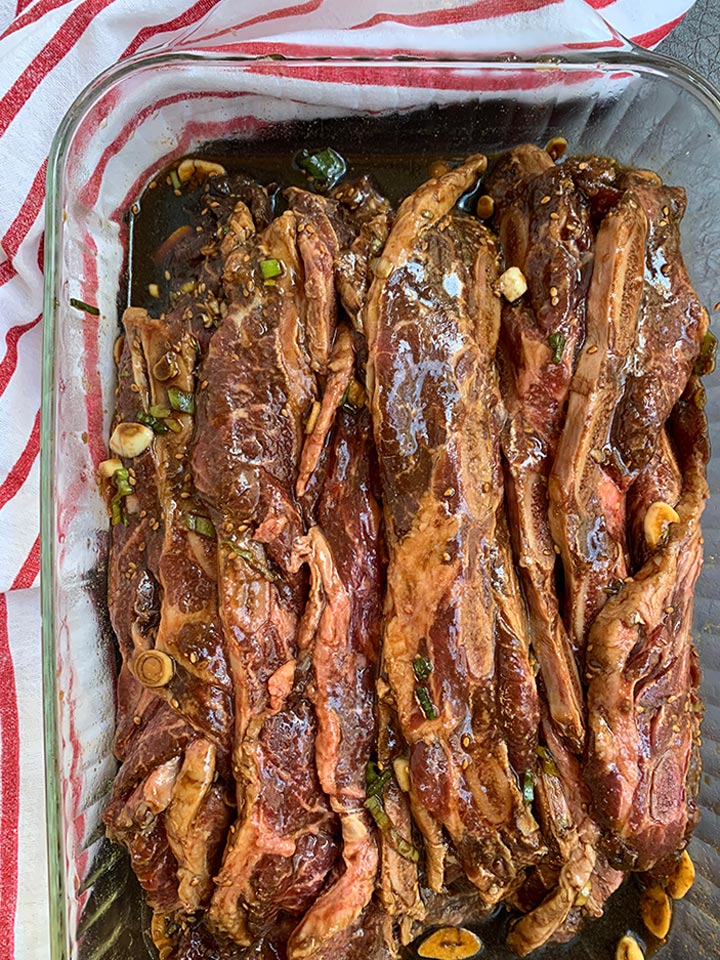 Kalbi ribs well marinated in glass 13x9 pan with red and white striped napkin.