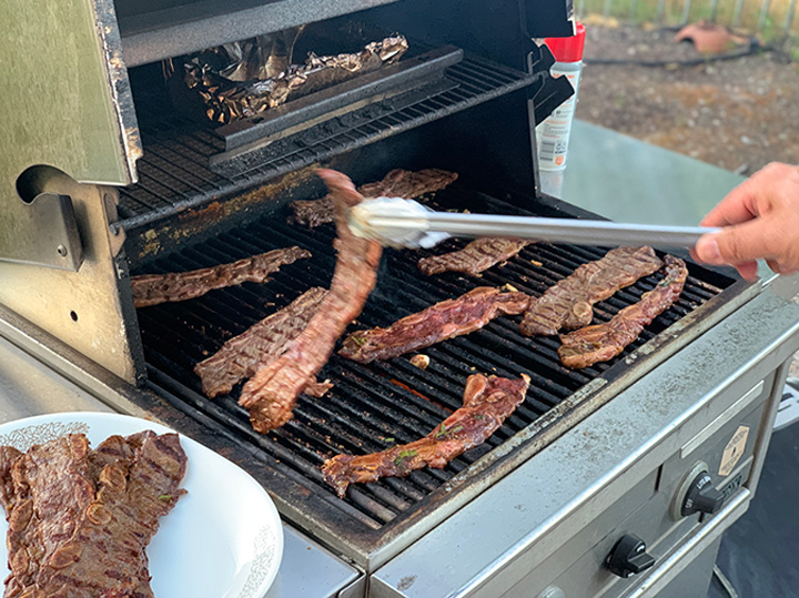 Short ribs on gas grill with being turned with tongs.