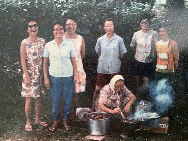 Grandma cooking kalbi ribs on Hawaiian beach with daughters in the background.