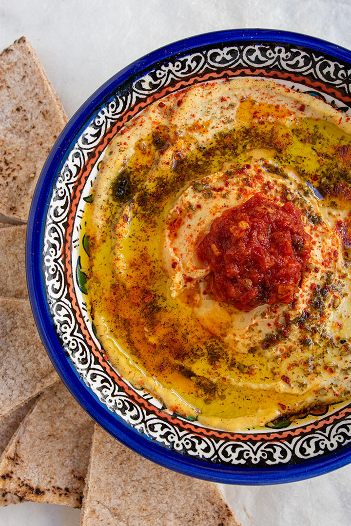 close up view of bowl of preserved lemon hummus with za'atar, marash pepper and harissa on top