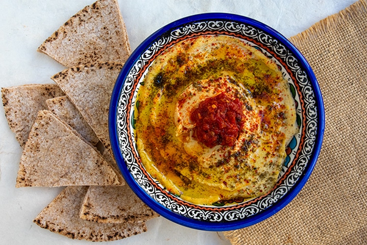 straight down shot of hummus with preserved lemons in blue bowl with pita chips on the left