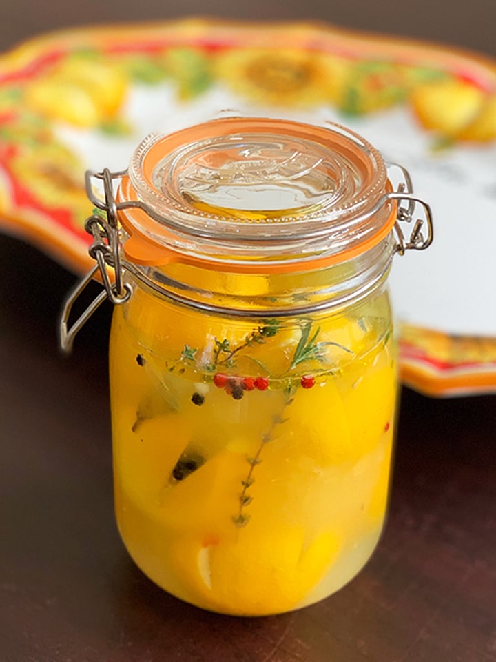 jar of preserved lemons ready to use and refrigerate with a lemony plate in the background
