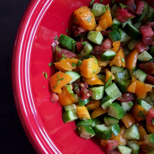 Tomato Cucumber salad in a red bowl on a black background.