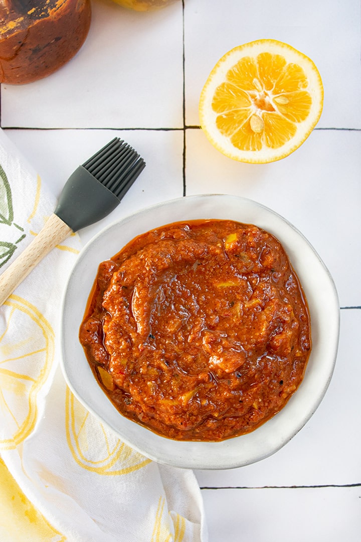 Harissa and preserved lemon sauce in white bowl with gray basting brush,