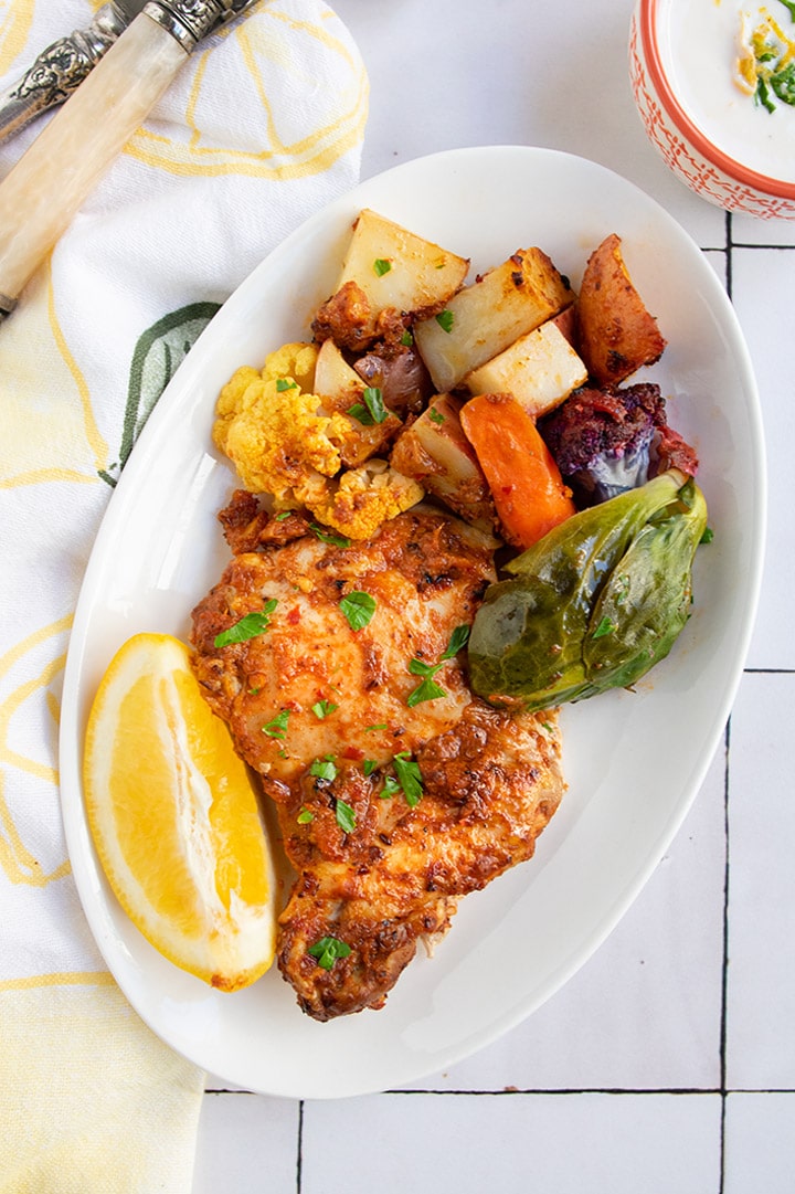 Harissa chicken with preserved lemons on white plate with roasted vegetables.