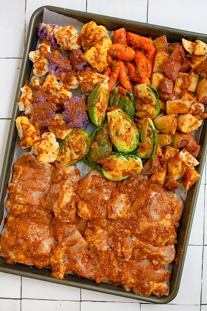 Chicken and vegetables brushed with harissa sauce on sheet tray.