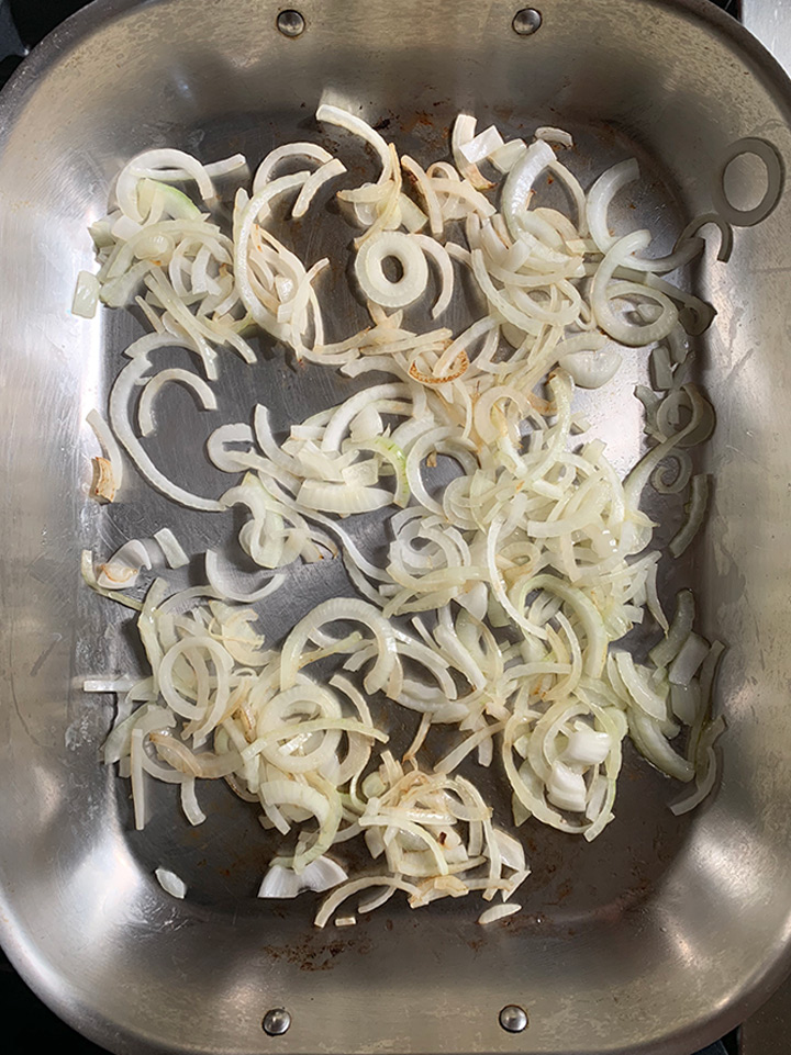 Fresh sliced onions browning in roasting pan.