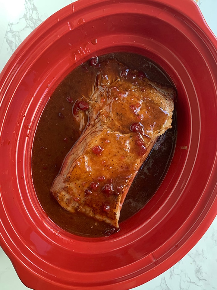 Uncooked brisket meat in red slow cooker with sauce poured over it.