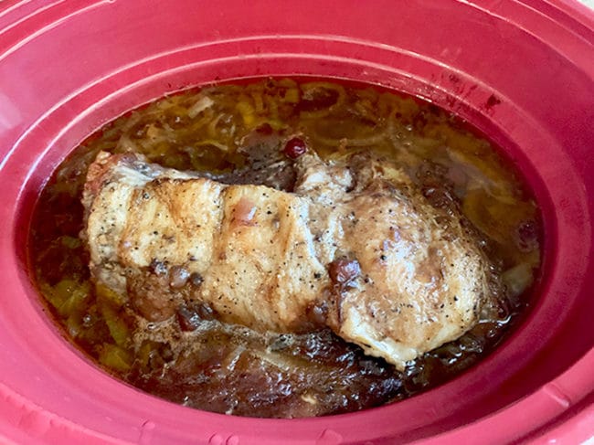 Partially cooked brisket meat in red slow cooker.