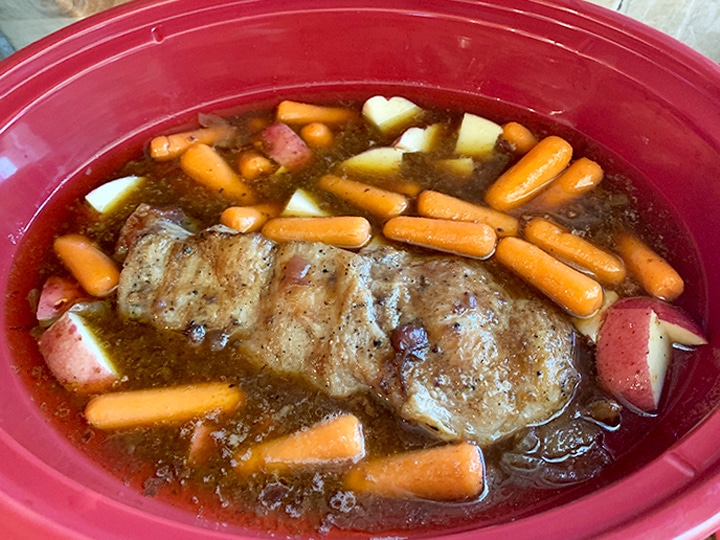 Carrots and potatoes added to slow cooker with brisket and sauce in the pot.