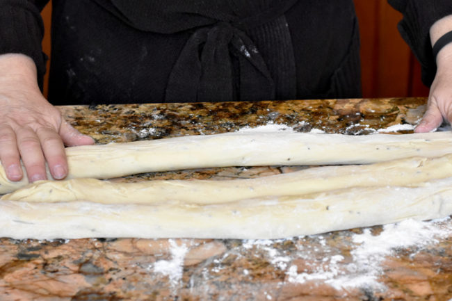 3 strands of challah dough on counter showing hands rolling them out.