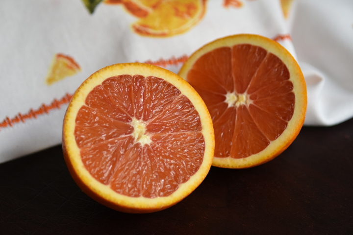 A sliced fresh cara cara orange with a white napkin decorated with oranges in the background.