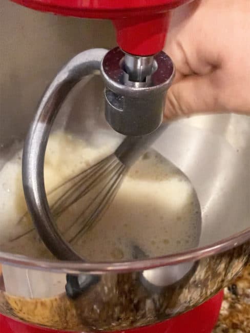 Eggs, oil, water and yeast in bowl of stand mixer being whisked by hand.