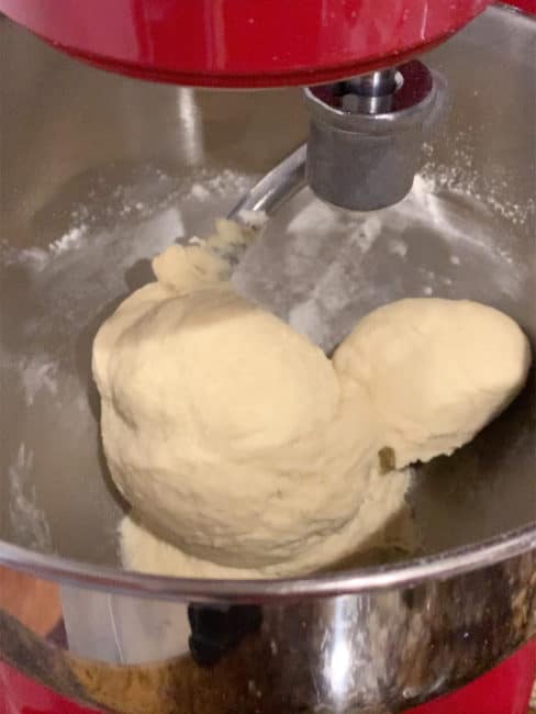 Challah dough in stand mixer fully kneaded and clinging to dough hook.