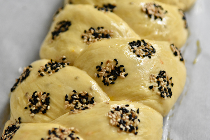 A close up of unbaked dough with decorative seed dots made up of sesame and nigella seeds.