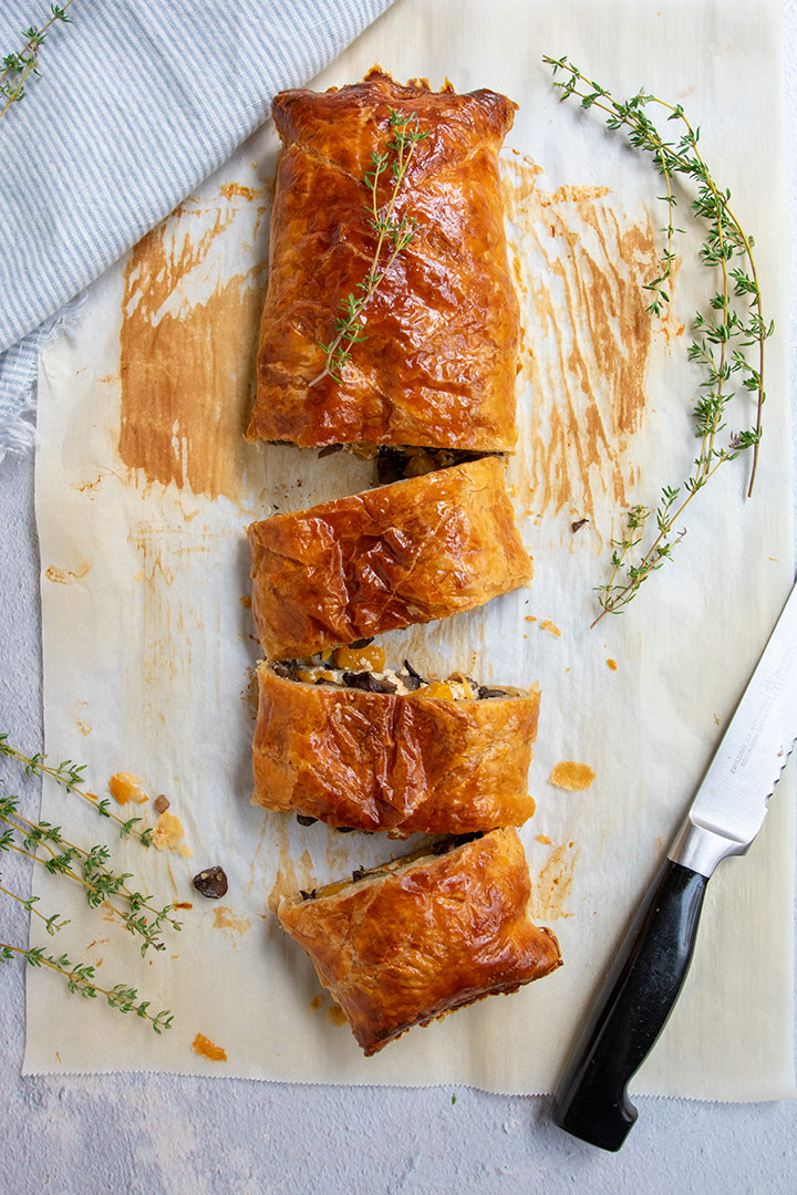 vegetable wellington with 3 slices on baked parchment with a serrated knife