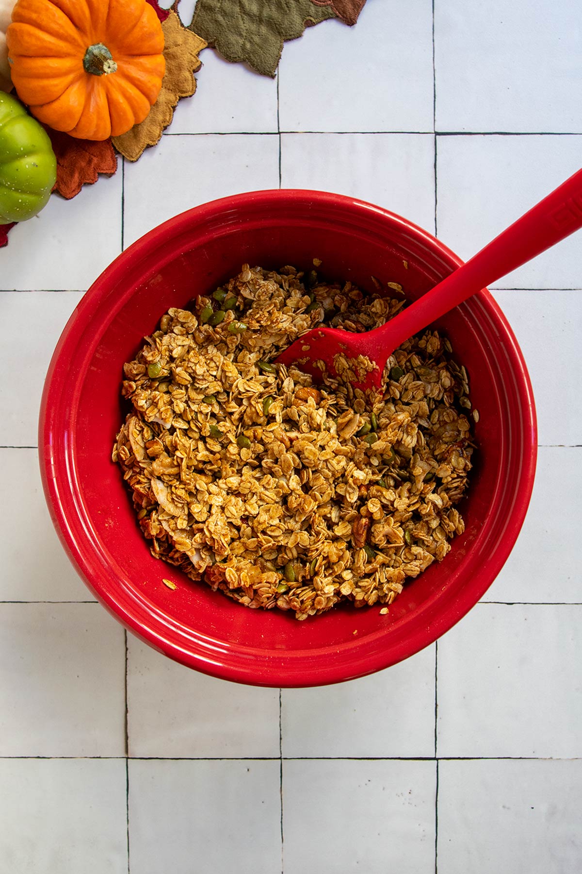 Wet and dry pumpkin granola ingredients mixed together in red bowl with red rubber spatula.