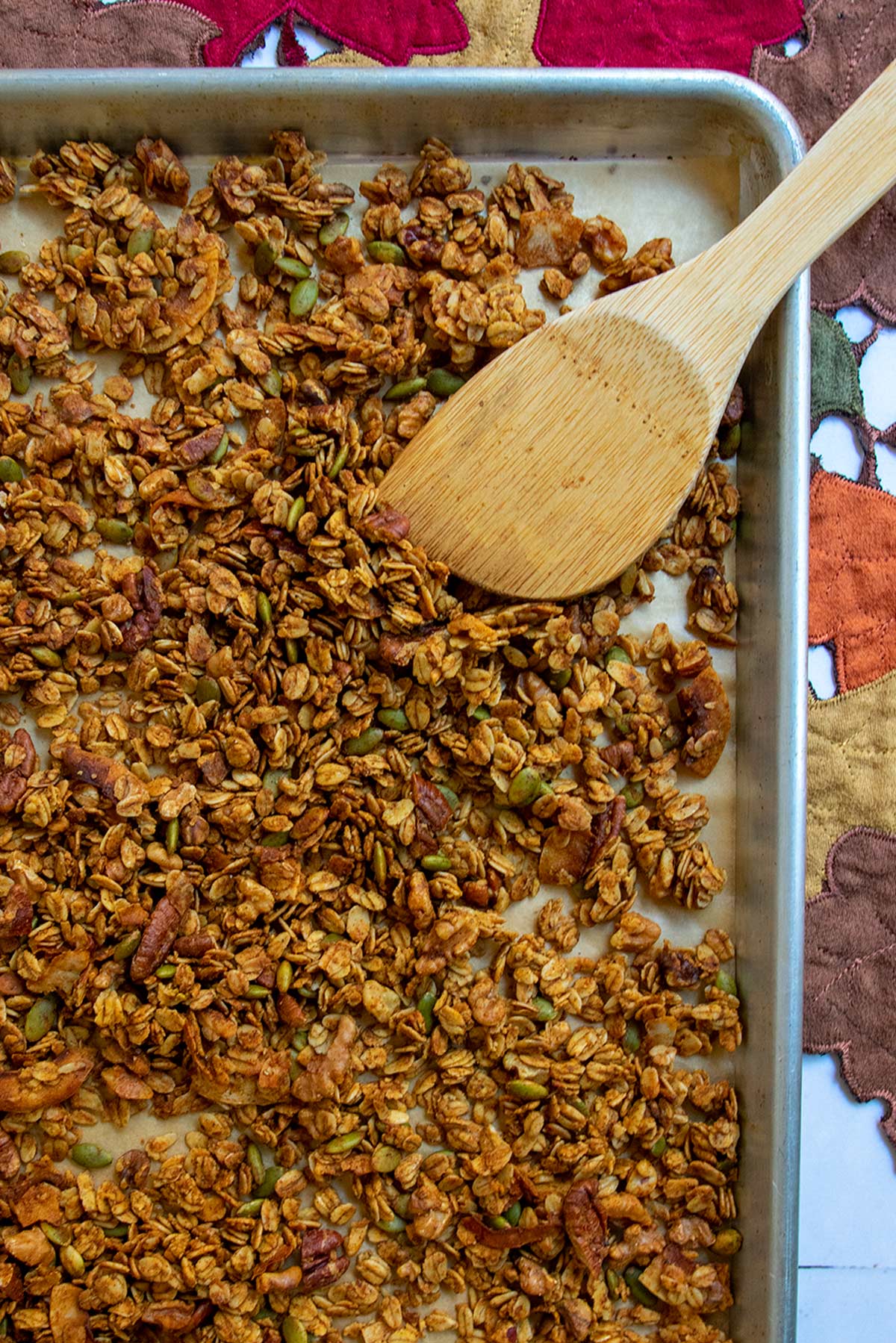 Baked granola on sheet tray with wooden mixing paddle.