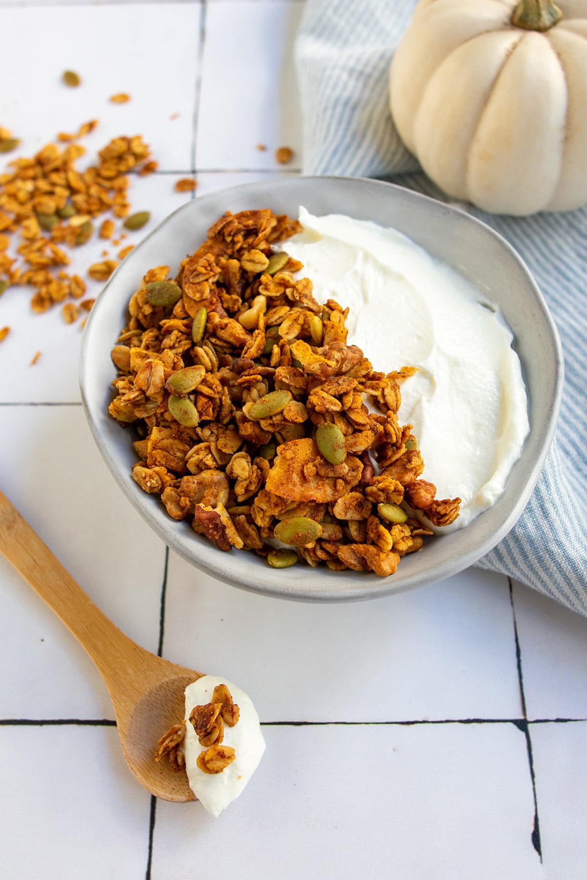 Yogurt and granola in grey bowl with white pumpkin and wooden spoon.