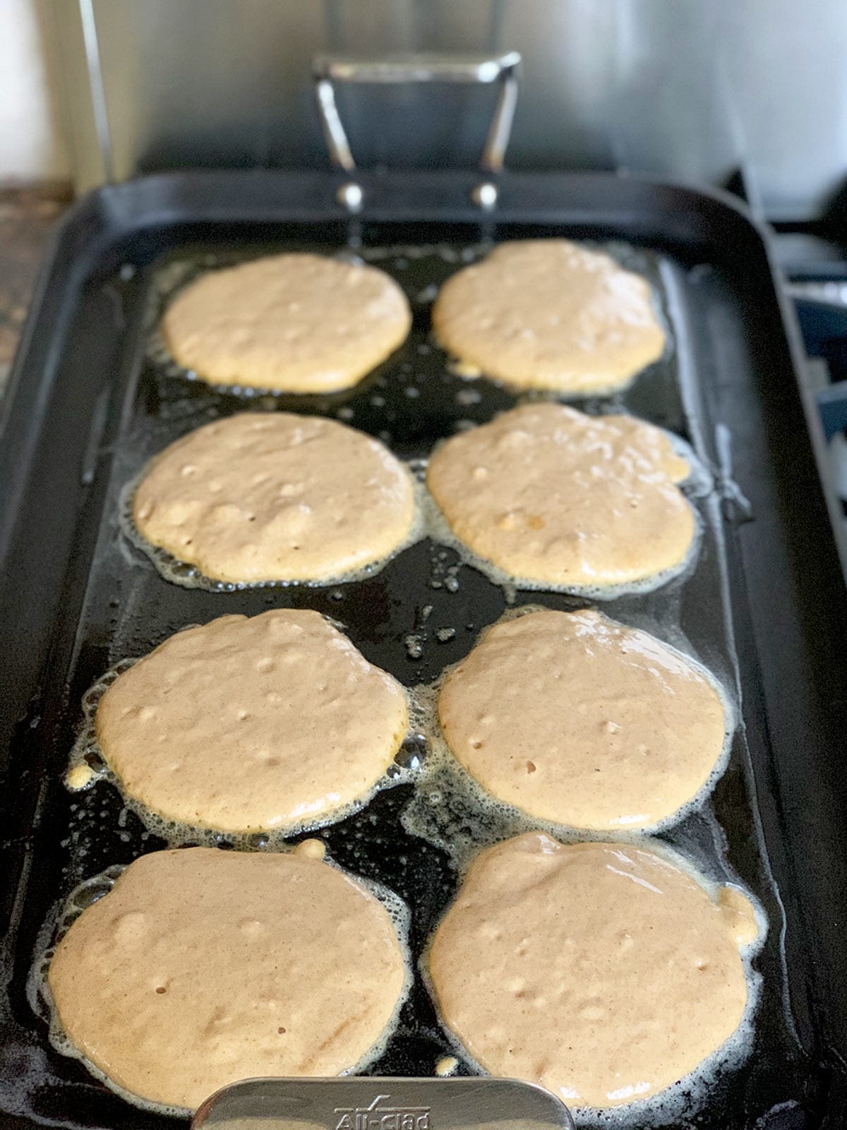 Pancakes cooking on griddle before being flipped.