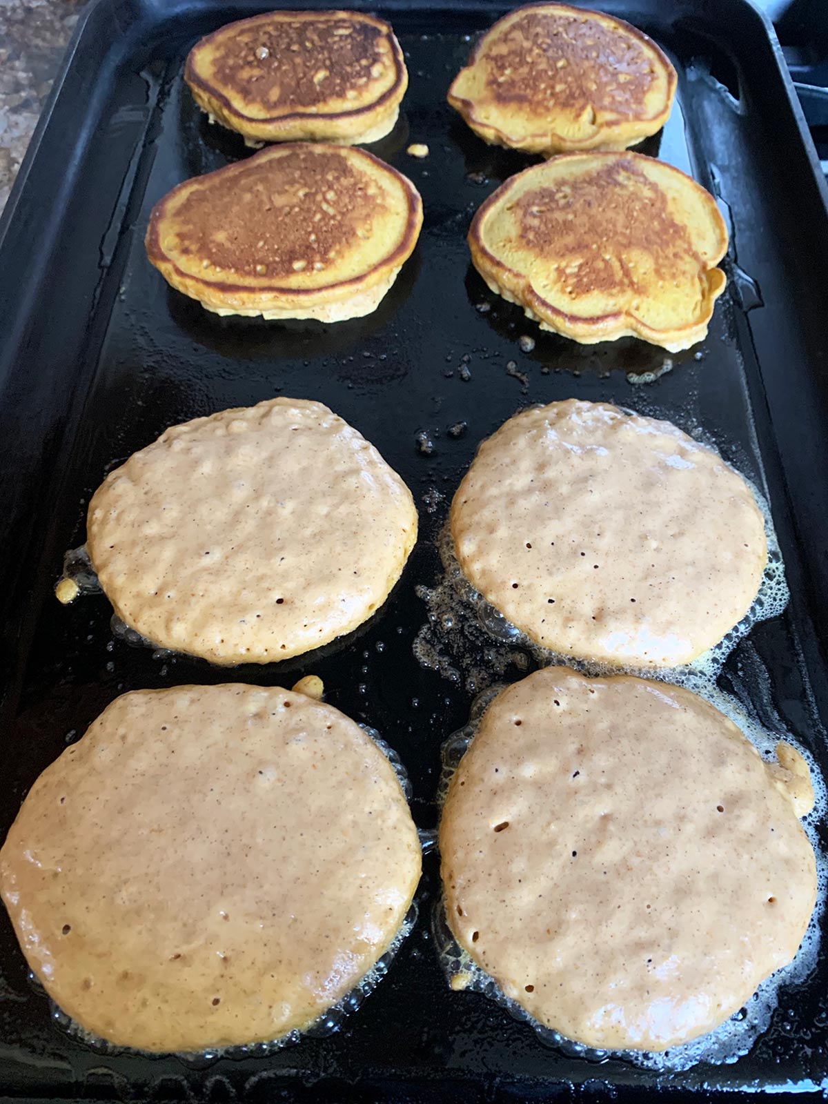 Pumpkin pecan pancakes on griddle half-turned and others showing little bubbles.