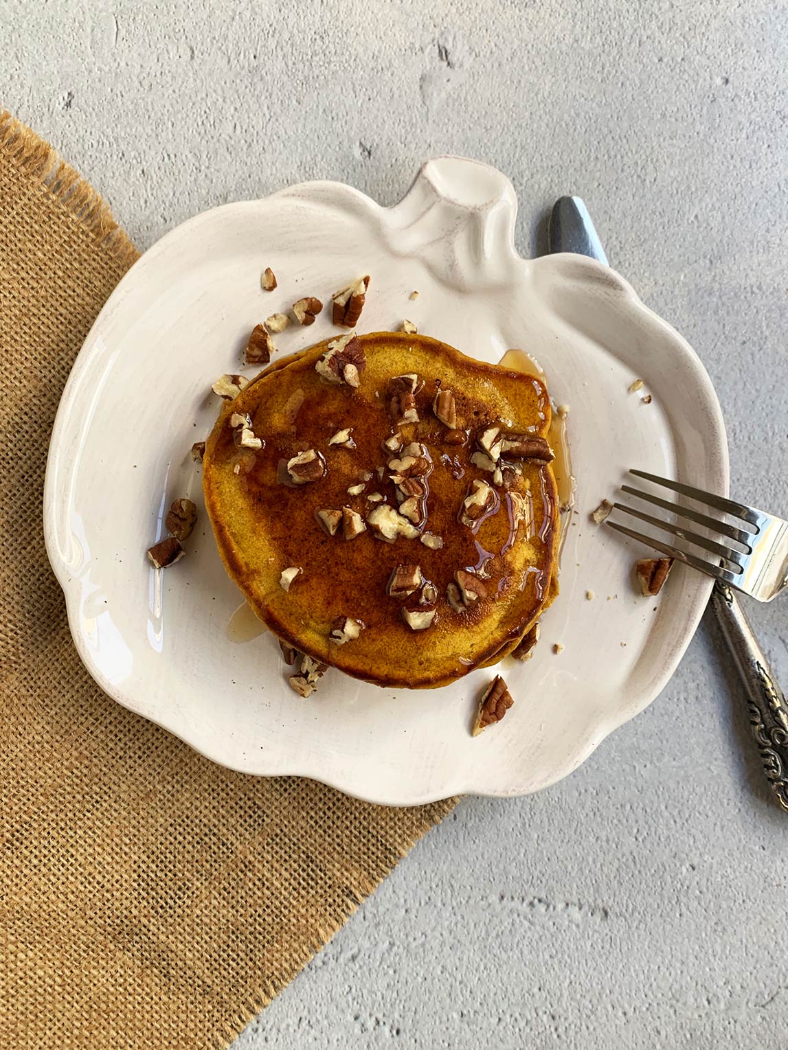 Stack of pumpkin pancakes on a pumpkin plate with pecans and syrup on top.