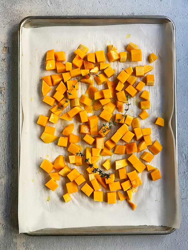 uncooked butternut squash on parchment paper-lined tray