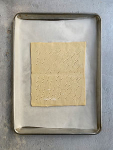 puff pastry with holes poked in it on a parchment lined sheet tray