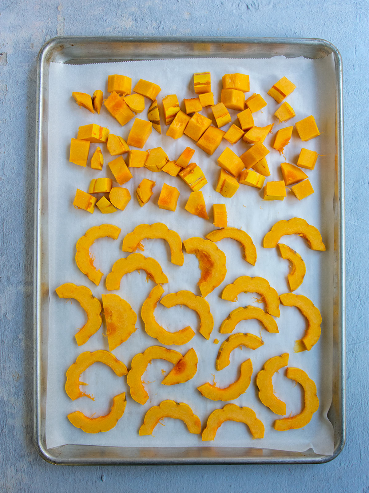 Cubed and half moon shaped squash on parchment lined sheet tray.