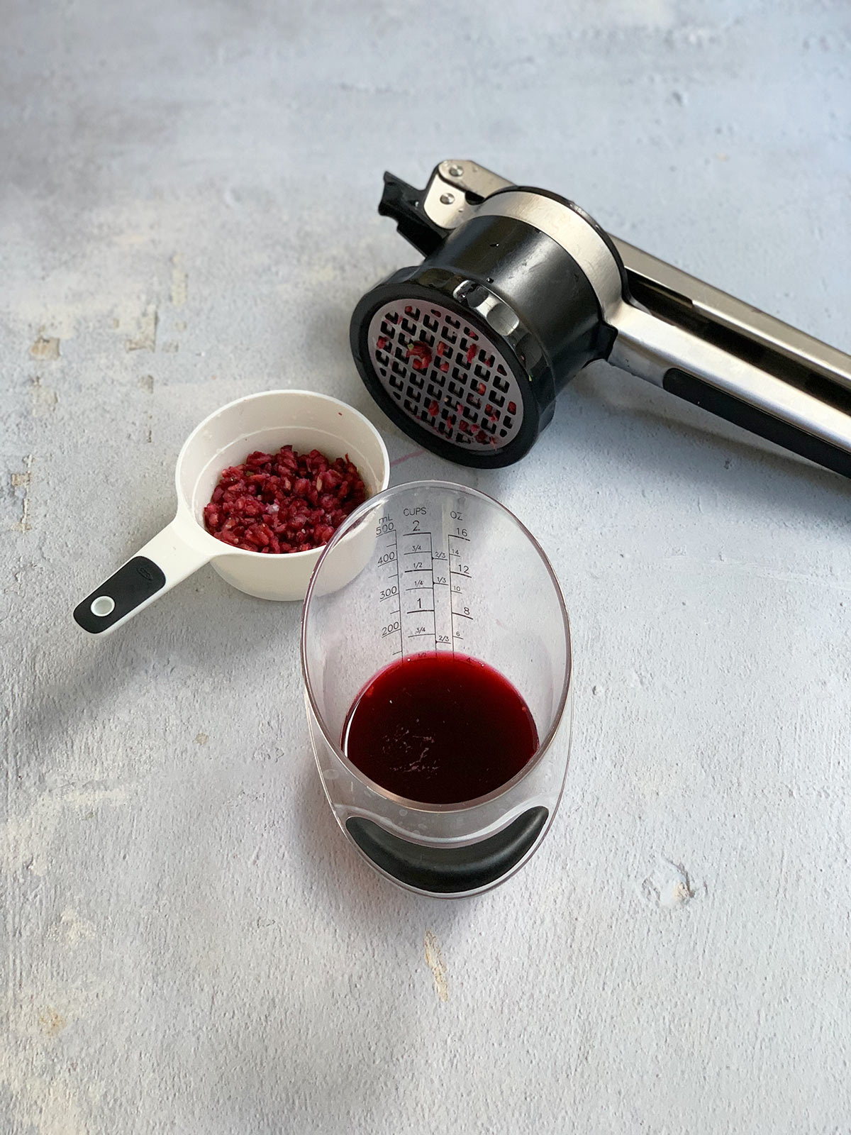 Fresh pressed pomegranate juice in a measuring glass with ricer and pressed seeds.