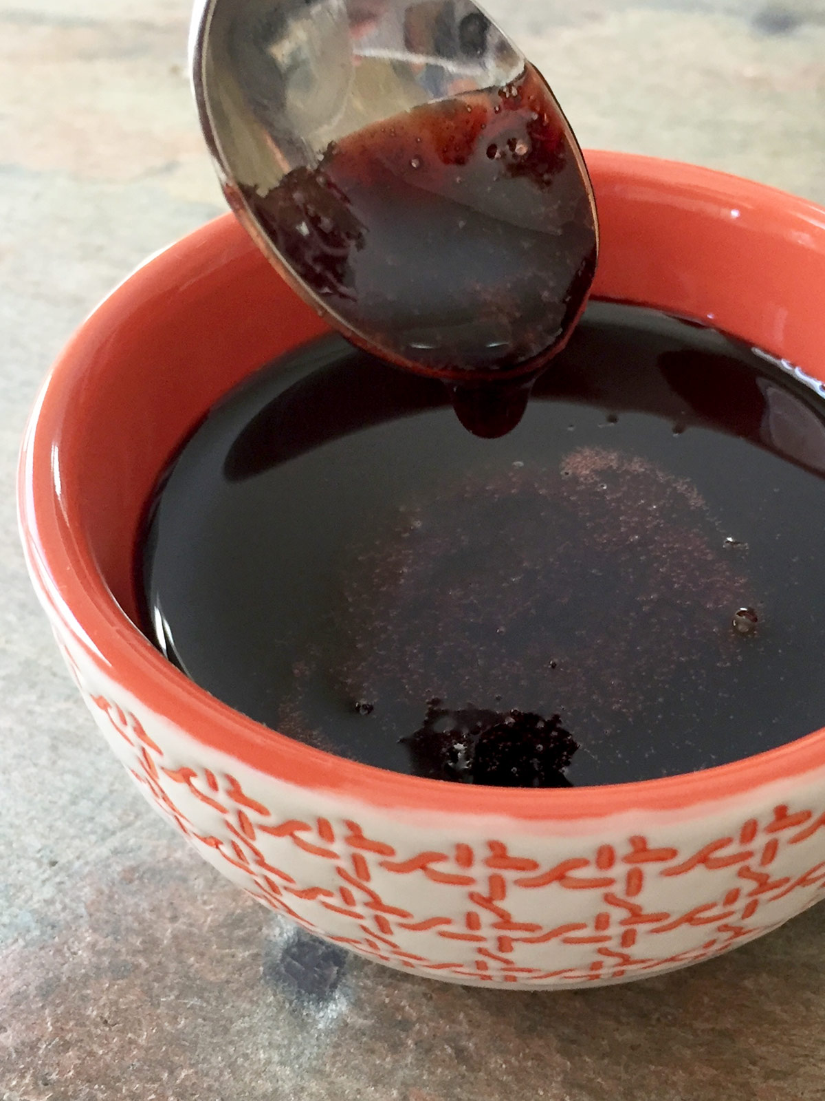 Pomegranate molasses dripping off spoon into orange bowl.