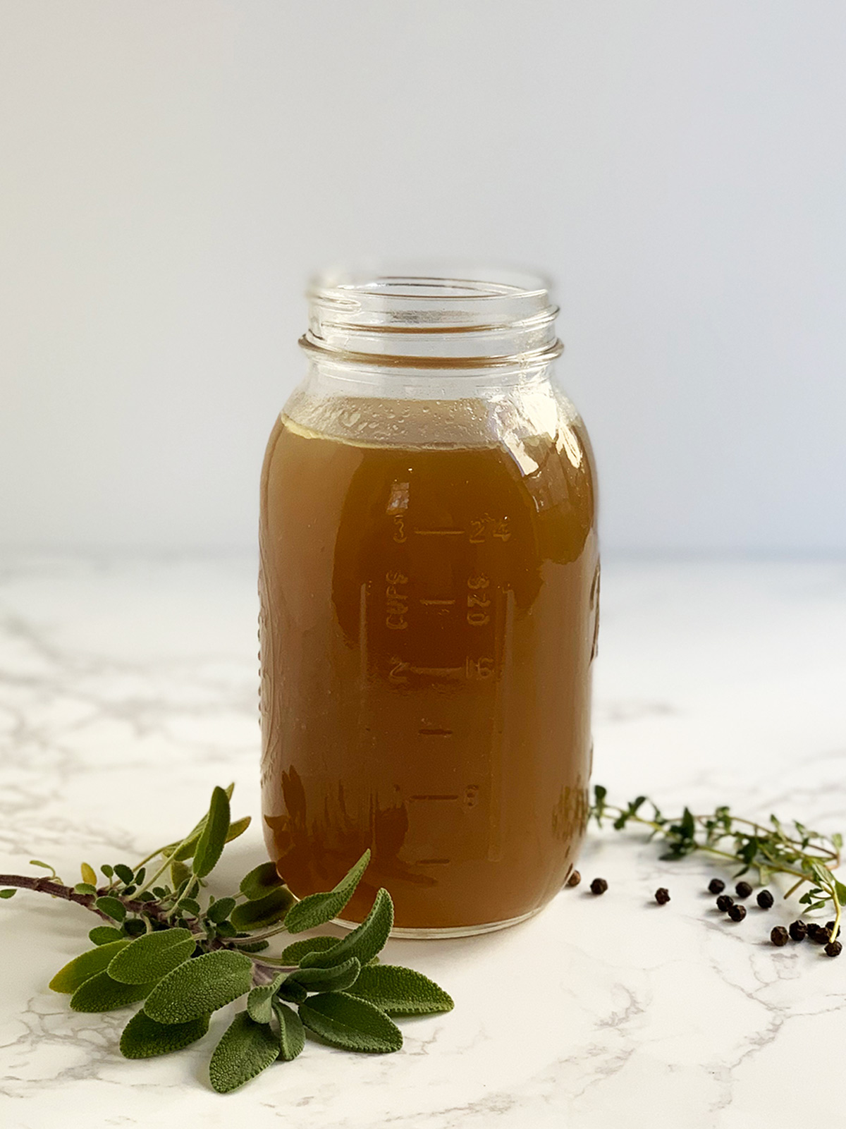 Turkey stock in glass jar with thyme, sage and peppercorns.