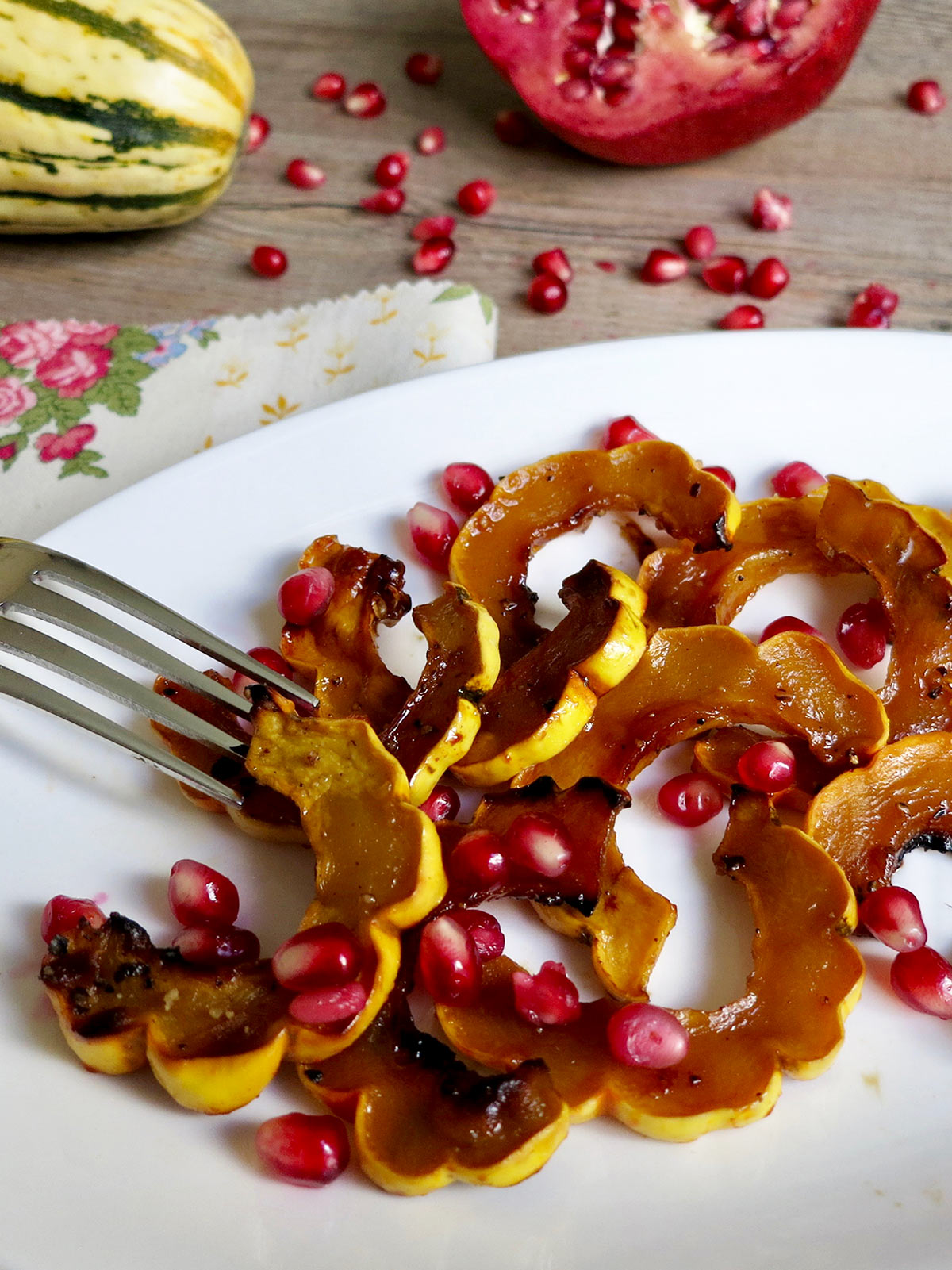 Roasted delicata squash on white plate with fork and pomegranate seeds.