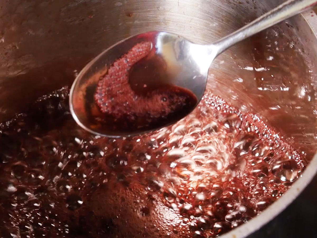 Boiling pomegranate juice with spoon showing the thickness of the liquid.